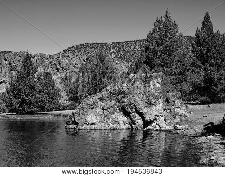 A giant partially submerged boulder extends from the shore into the waters of Prineville Reservoir in Central Oregon on a clear summer morning.