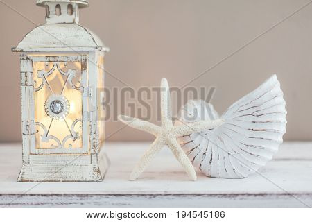 Beach wedding interior decor. Natural seashell and lantern on vintage shelf over pastel wall.