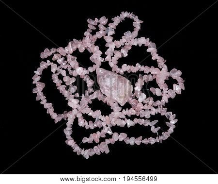 Tumbled rose quartz stone surrounded by rose quartz strings on black background
