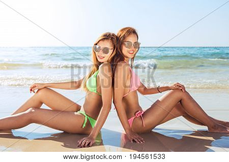 Two sexy women in bikinis on the sunny beach. Best friends having fun Summer vacation holiday lifestyle. Happy women relaxing freedom on white sand.