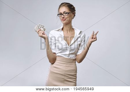 A business lady in glasses and white shirt holds a little money in her right hand and her left hand shows that there is very little money. The concept of a small salary an inadequate remuneration or bad economics or crisis.