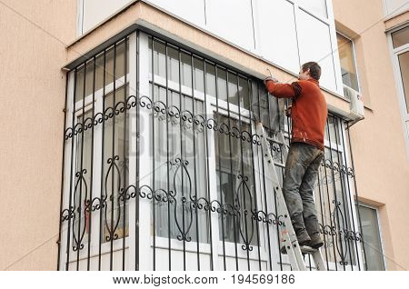 KYIV UKRAINE - AUGUST 16, 2017:  Worker install window iron security bars for house safety. Contractor installing window iron security bars with welding. Security Shutters Grilles Installation.