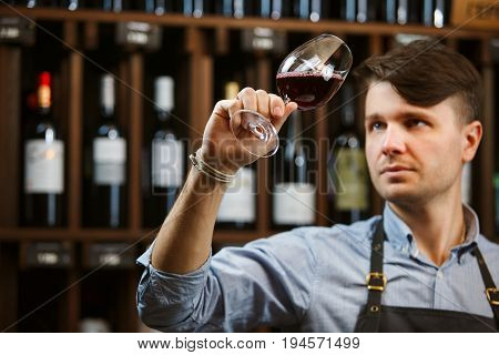 Bokal of red wine on background of male sommelier appreciating color, quality, flavor and sediments of drink. Professional degustation expert in winemaking.