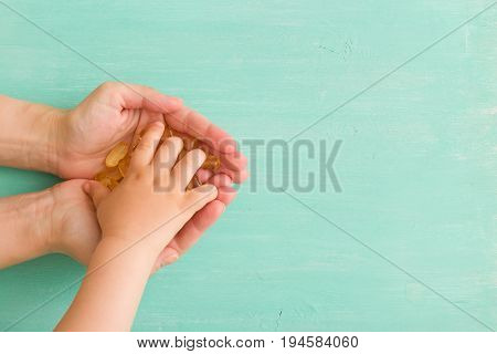 Top view on child's hand taking capsules Omega 3 from mother's hands on turquoise background. fish fat oil capsules. Health concept