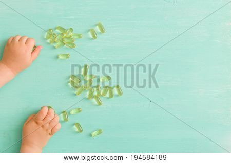 Top view on child's hands taking capsules Omega 3 on turquoise background.
