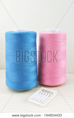 spools of thread of blue and pink and pack of needles for sewing machines