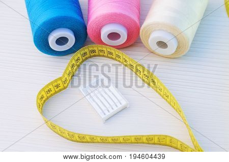 spools of sewing thread, blue, pink, beige, pack of needles for sewing machines and tailor's meter heart