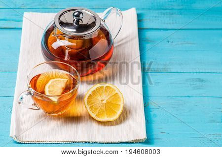 Glass cup of tea with lemon and glass teapot on blue wooden table.