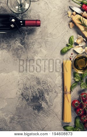 Italian food background with ravioli, vine tomatoes, basil, spaghetti, spinach, onion, parmesan, olive oil, garlic, peppercorns, rosemary and wine. Slate background 
