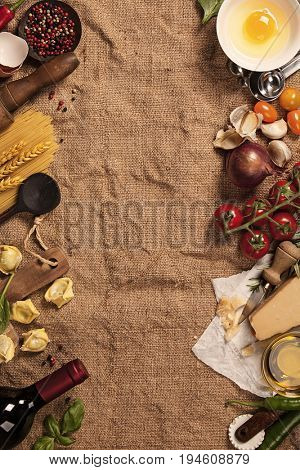 Italian food background with vine tomatoes, basil, spaghetti, spinach, onion, parmesan, olive oil, garlic, peppercorns, rosemary and eggs. Burlap background