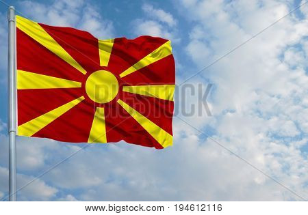 National flag of Macedonia on a flagpole in front of blue sky.