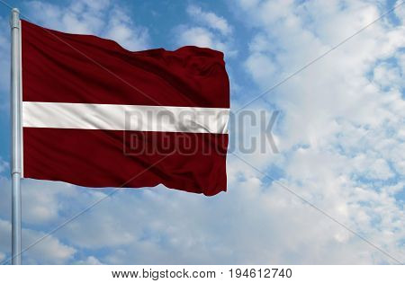 National flag of Latvia on a flagpole in front of blue sky.