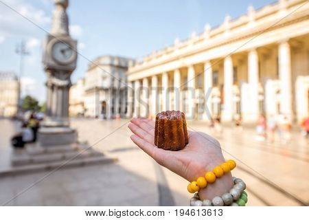 Holding a traditional Bordeaux sweet cake called Canele outdoors on the street near the Grand theatre building in Bordeaux