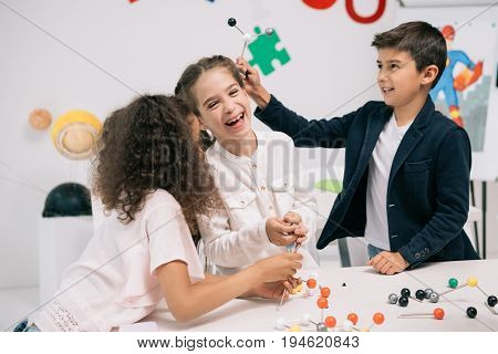 Adorable multiethnic schoolchildren working with molecular model and smiling in class