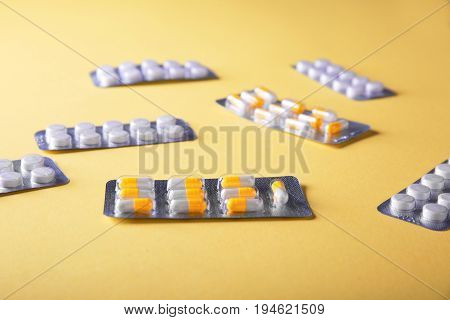 Packaging for drugs: antibiotics, painkillers, vitamins and aspirin tablets. Set of white blisters realistic icons with pills and capsules scattered on a yellow background.