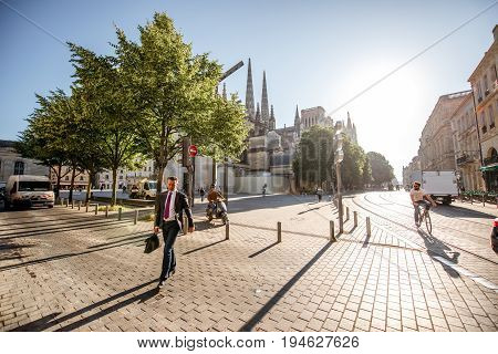 BORDEAUX, FRANCE - May 24, 2017: Businessman cross the street with saint Pierre cathedral on the background during the sunny morning in Bordeaux city, France