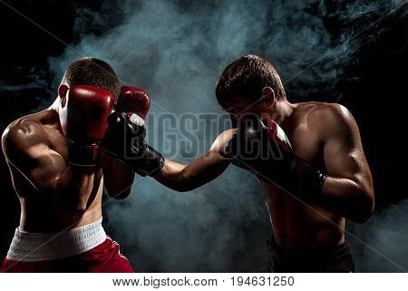 Two professional boxer boxing on black smoky studio background.