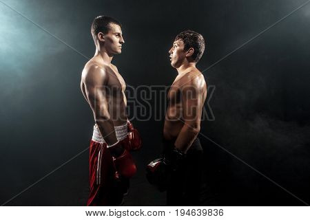 Two professional boxer standing on black smoky studio background.