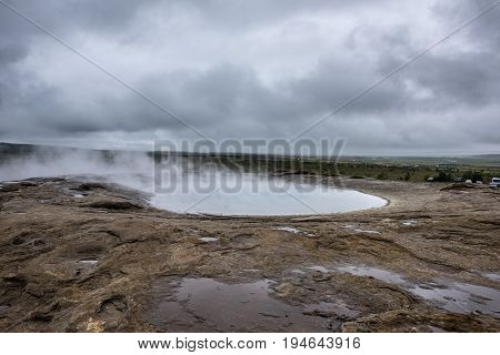 Natural Hot Springs geyser in Iceland. Steam rises from the Icelandic hot springs on a gloomy summer day