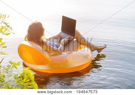 Young Woman Working On A Laptop In The Water On An Inflatable Ring, Copy Space For Your Text. Work O