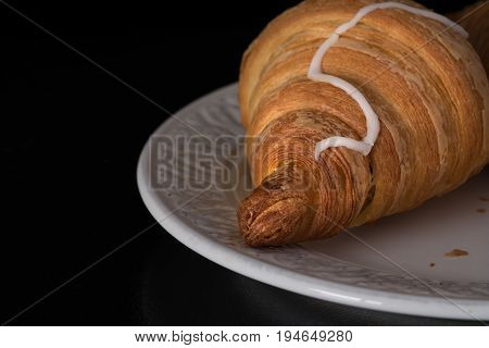 Cinnamon crescent croissant close up view on white plate on the black background