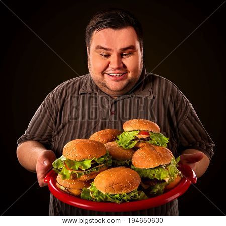 Fat man eating fast food hamberger and carries treat for friends on tray. Breakfast for overweight person. Junk meal leads to obesity.
