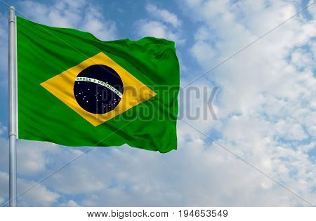 National flag of Brazil on a flagpole in front of blue sky.