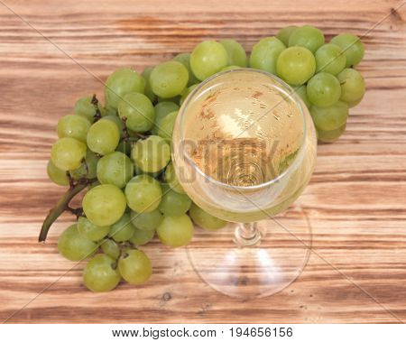 Glass of white wine and ripe organic green grapes isolated on vintage wooden background