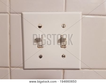 two white lightswitches in front of white bathroom tiles