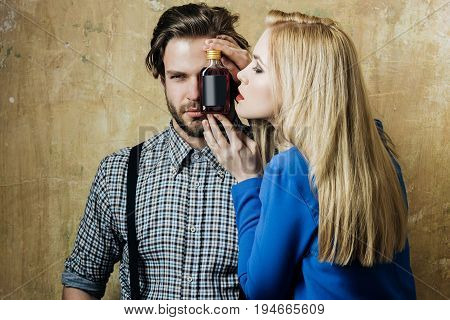 Girl and macho posing with liqueur bottle. Adorable woman with blond long hair and handsome man on beige background. Alcohol appetizer addictive and convive. Unhealthy lifestyle and bad habits