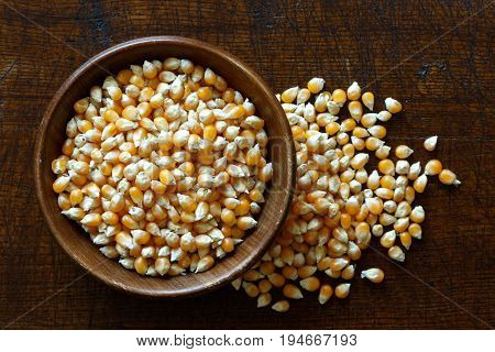 Unpopped Popcorn In Dark Wooden Bowl Isolated On Dark Brown Wood From Above. Spilled Popcorn.
