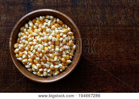 Unpopped Popcorn In Dark Wooden Bowl Isolated On Dark Brown Wood From Above.