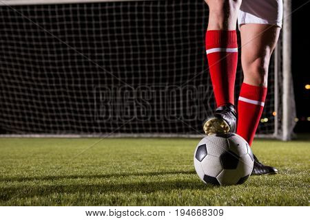 Low section of male soccer player with ball on field against goal post