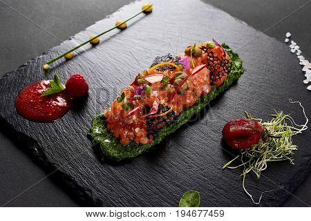 fresh salmon tartar with salt and herbs, studio shot. Fish tartar on black shale