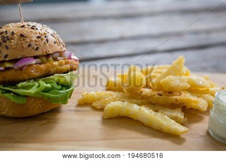 Close up of burger and french fries with dip on cutting board