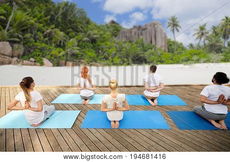 fitness, sport, yoga and healthy lifestyle concept - group of people exercising in reverse prayer pose over tropical beach background