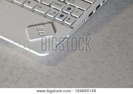 A Compact Sd Memory Card Lies On A White Netbook. The Digital Information Storage Device Is Ready Fo