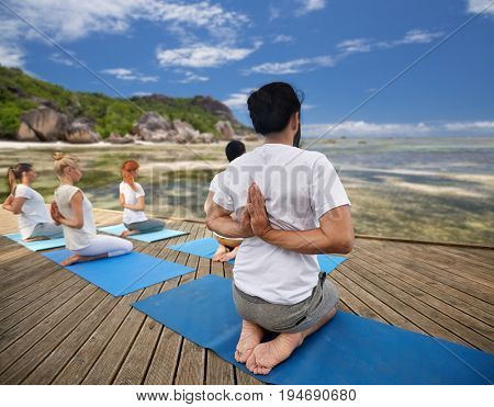 fitness, sport, yoga and healthy lifestyle concept - group of people exercising in reverse prayer pose over exotic tropical beach background
