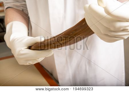 Artisanal production of caramel toffee sweets butterscotch candies. Woman with white lab coat blouse stretching moving extending the sugar pastry to do butterscotch candies sweet of France