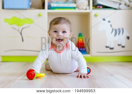 Cute happy smiling baby playing with colorful rattle toys. New born child, little girl looking at the camera and crawling. Family, new life, childhood, beginning concept. Baby learning grab