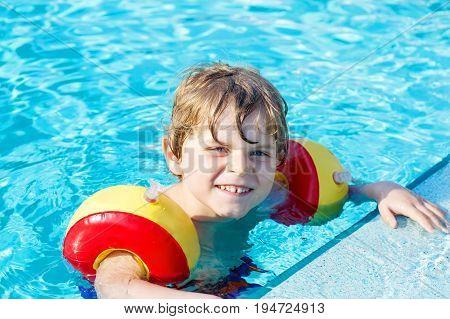 Happy little kid boy having fun in an swimming pool. Active happy child learning to swim. with safe floaties or swimmies. Family, vacations, summer concept.