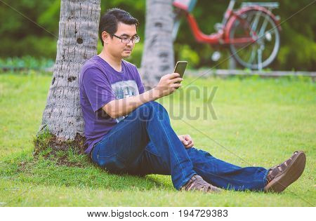 Asian man sitting and play his mobile phone in the park
