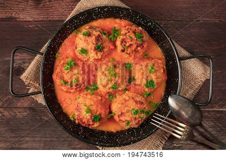 An overhead photo of meatballs in tomato sauce, shot from above in the skillet on dark rustic textures, with a fork and a spoon, and a place for text