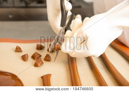 Artisanal production of caramel toffee sweets butterscotch candies. Woman with white lab coat blouse cutting rolls of sugar pastry to do butterscotch candies traditional sweetx of France