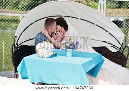 Beautiful Wedding Couple Enjoying Each Other's Comany On A Bench On A Lakeside.