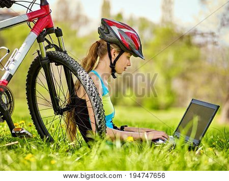 Woman traveling bicycle in summer park. Bicyclist girl watch on laptop. Girl counts pulse after sport training and is looking for way to navigator. Dependence on social networks. Person makes money on
