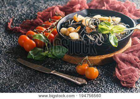 Black spaghetti with prawns and scallop in frying pan on black background