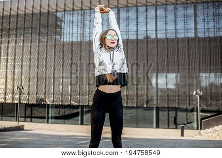 Lifestyle portrait of a stylish woman in silver jacket exersicing outdoors in the modern urban environment