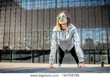 Lifestyle portrait of a stylish woman in silver jacket exersicing outdoors in the modern urban environment