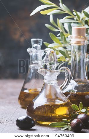 Olive oil in a glass bottle and olive branch on brown stone table